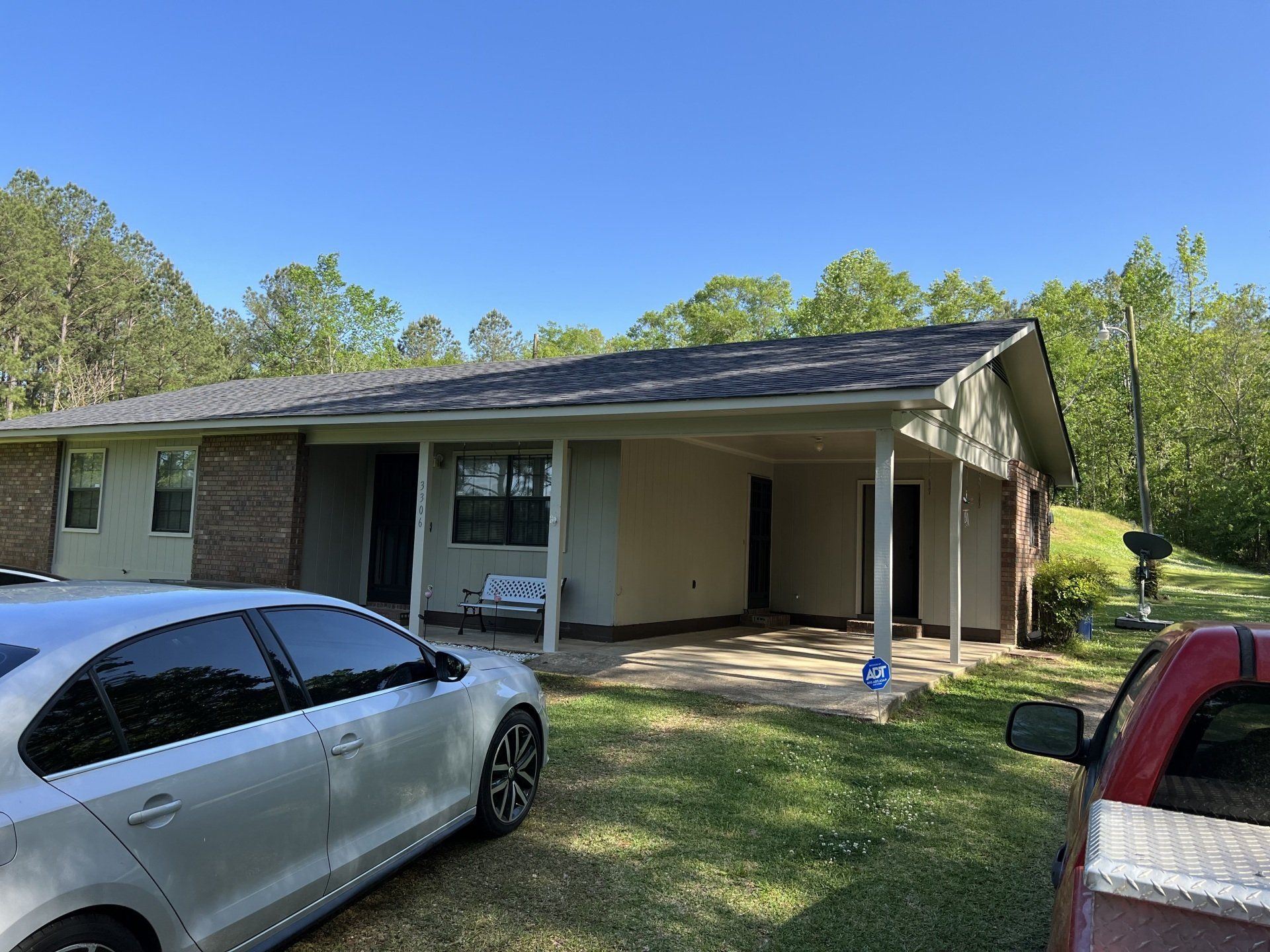 Single-story house with carport, silver sedan in front, and a red vehicle at the edge of the yard.
