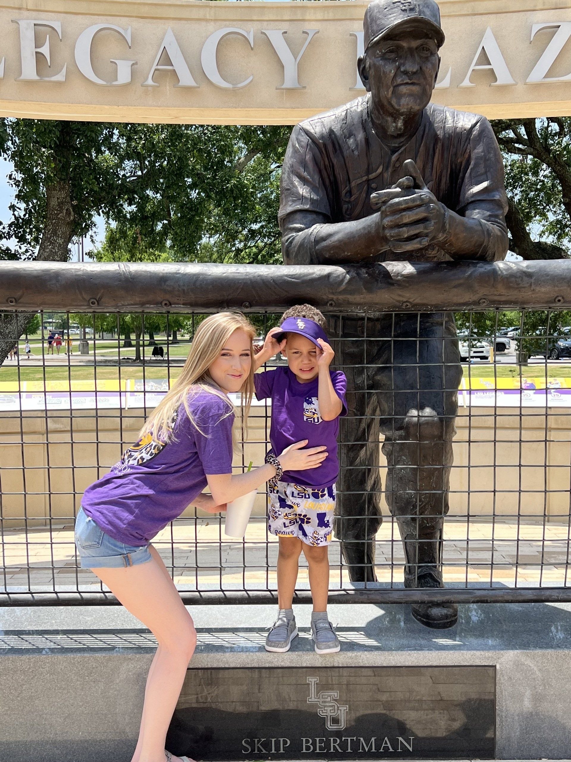 Two children pose with a bronze baseball player statue at a park sign.
