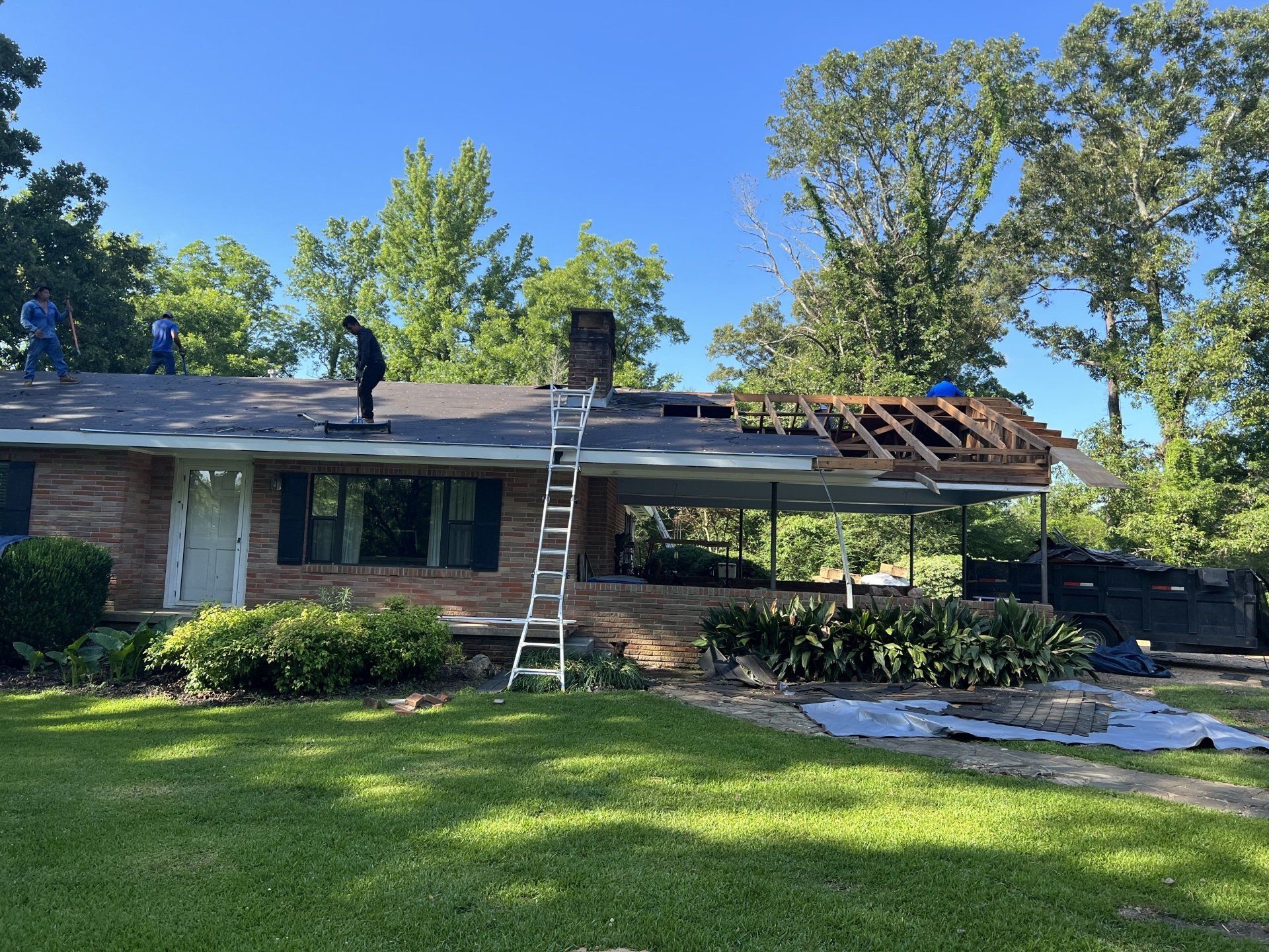 Workers repairing a house roof with ladders in a sunny suburban yard