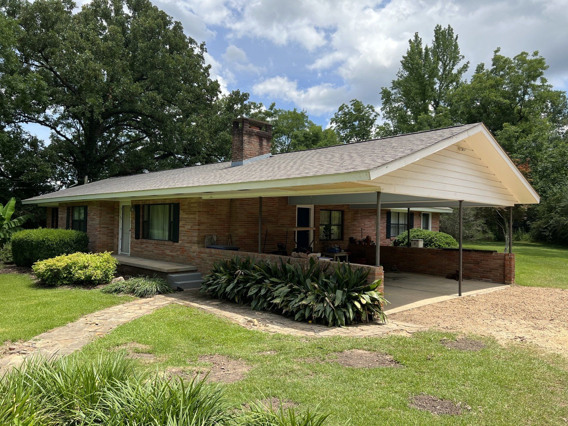 Single-story brick house with a covered porch, surrounded by trees and a gravel driveway