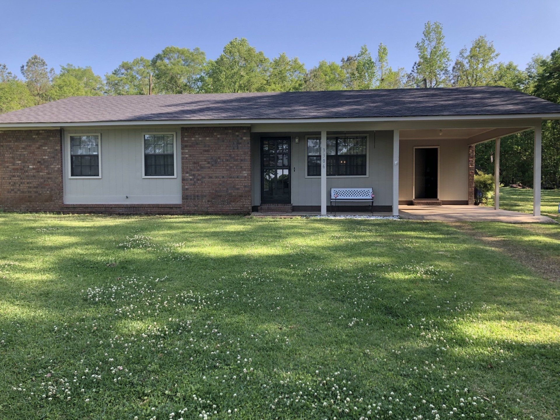 Single-story brick house with a covered porch and large front lawn on a sunny day