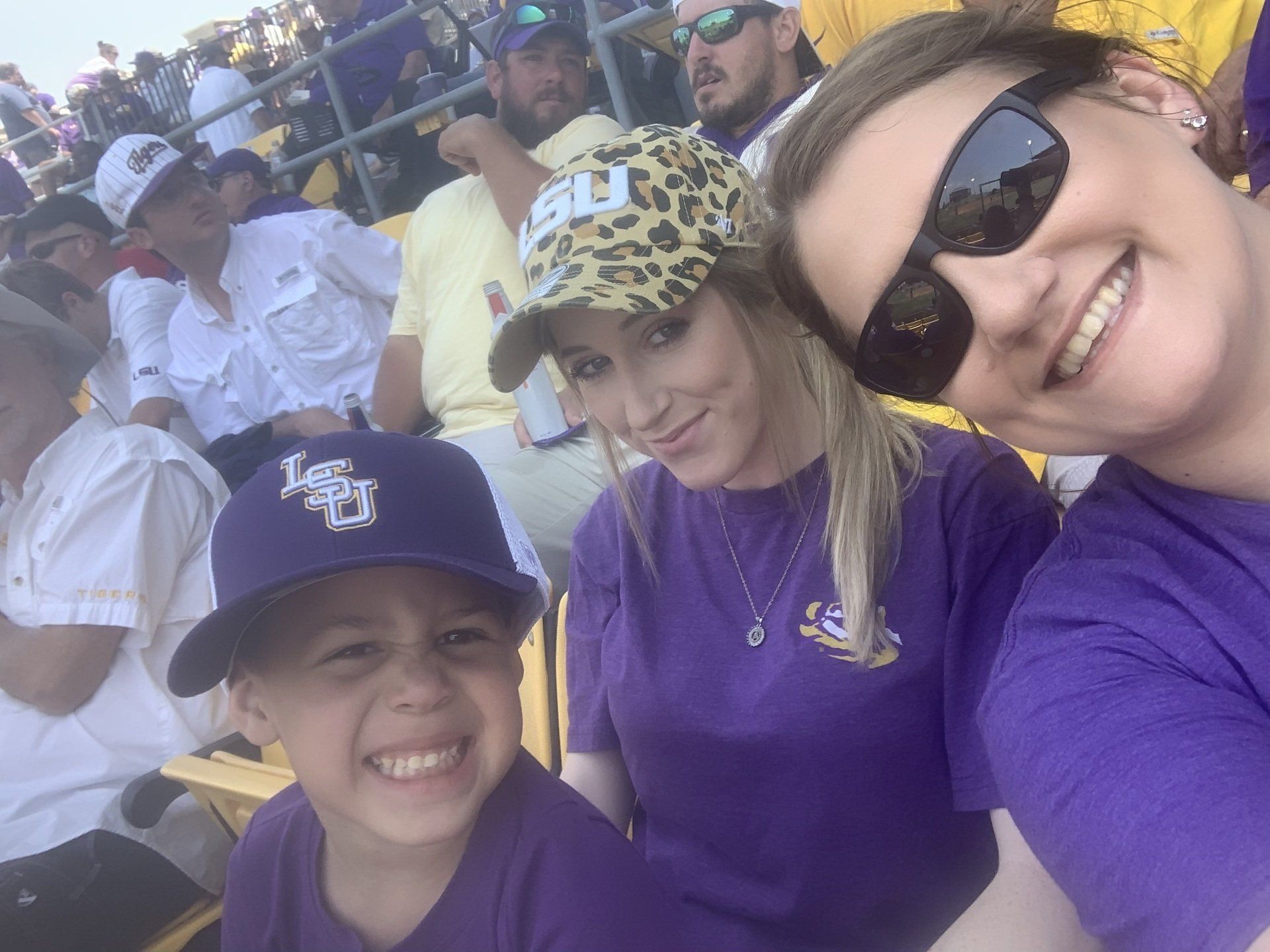 Three people in purple shirts and caps smiling at an outdoor event seating area.