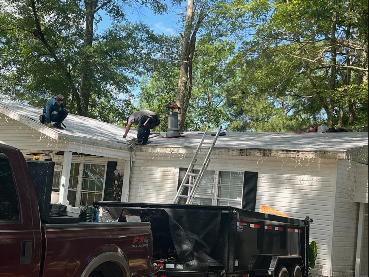 Workers on a white house roof with a ladder and dumpster, removing or repairing shingles