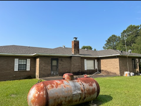 Single-story brick house with a large rusted propane tank in the front yard under a clear blue sky