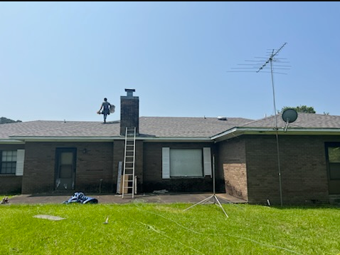 Single-story brick house with a ladder against the chimney and a satellite antenna on the roof above a green lawn.
