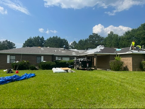 Damaged house roof with tarp and debris on a sunny lawn after storm