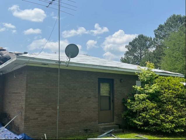 Brick house side with satellite dish, door, and bushes under a blue sky