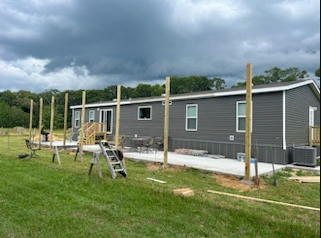 Mobile home under construction with gray siding, wooden posts, and a cloudy sky.