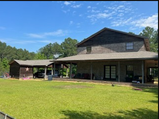 Large rustic house with a covered porch and green lawn under a blue sky