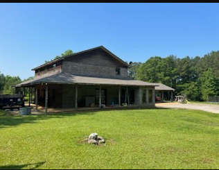Rustic two-story barn-style house with a wraparound porch on a sunny grassy lot