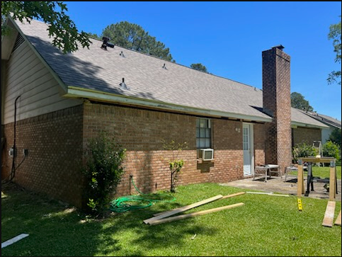 Backyard view of a brick house with a sloped roof, chimney, and lawn under a clear blue sky