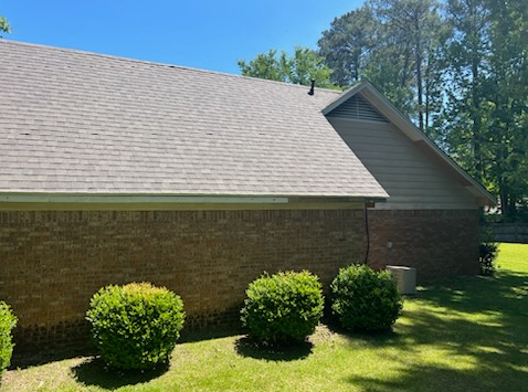 Brick house with gray roof, trimmed shrubs, and trees under a clear blue sky