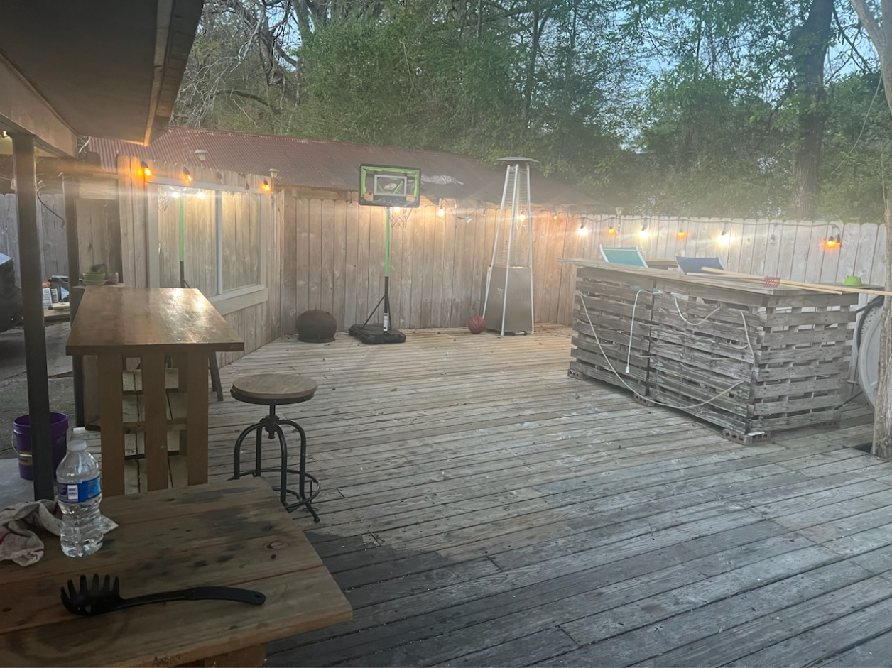 Backyard deck with string lights, stools, tables, and a basketball hoop at dusk