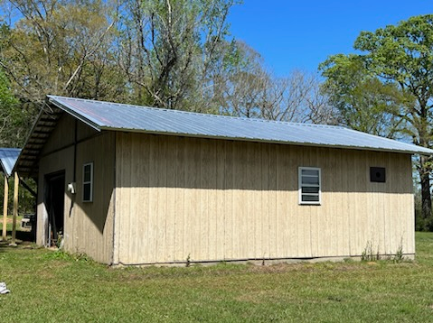 Small beige metal building with a gray roof, set on a grassy lot under a blue sky.