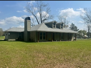 Single-story gray house with a covered porch and chimney on a grassy lot under a blue sky