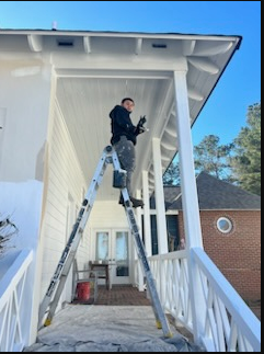 Person on ladder painting white house entryway under roof overhang