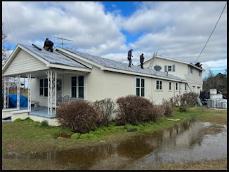 Workers on a house roof installing solar panels beside a flooded roadside