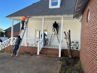 Workers painting a house porch, one on a ladder and another on the ground beneath the white awning