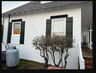 White house exterior with green shutters, a gas tank, and shrubs by the front window.