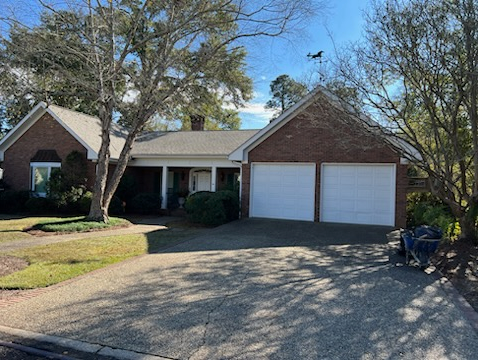 Brick suburban house with two white garage doors, curved driveway, and trees in front yard