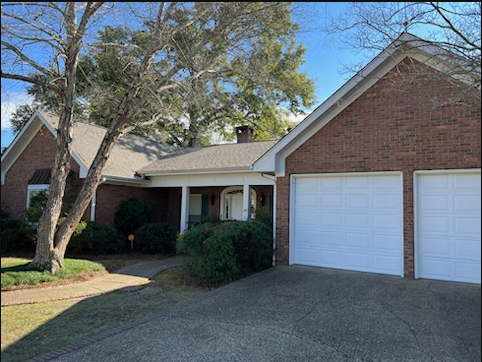 Suburban brick house with two white garage doors, front porch, and large tree in the yard