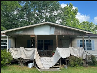 Front porch of a house with draped white sheets and a porch swing under trees