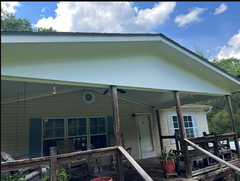 White house porch with wooden railings and potted plants under a gabled roof on a sunny day