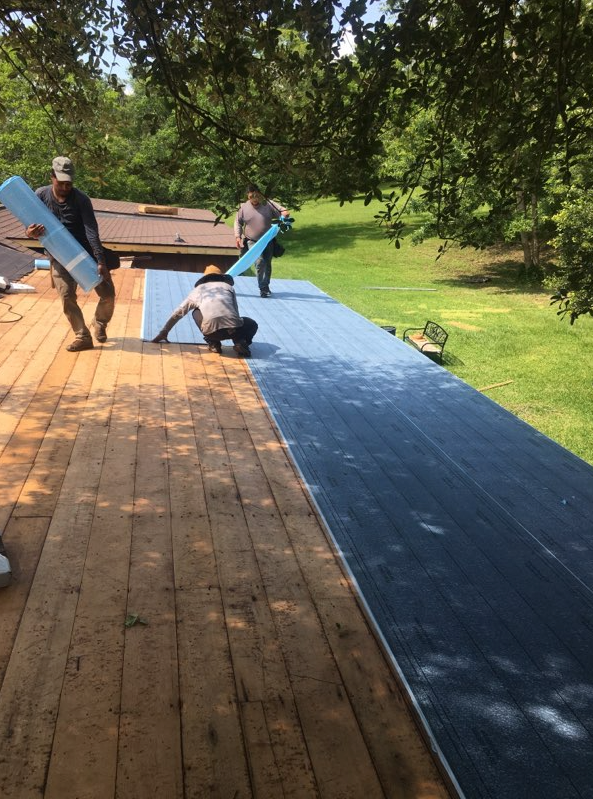 Workers installing blue roofing on a wooden roof under trees