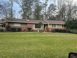 Single-story brick house with a large front lawn and trees in the background