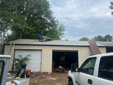 Workers repair a roof on a beige garage with open bay doors and debris in front.