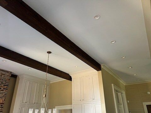 White kitchen ceiling with dark wood beams, recessed lights, and tall cabinets near a hanging pendant lamp