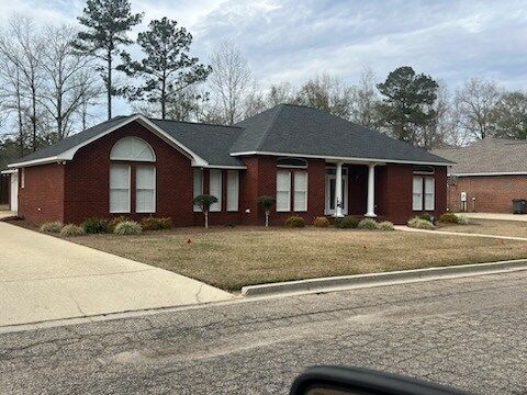 Single-story red brick house with white columns and a dark roof on a suburban street