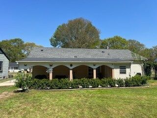 Single-story brick house with arched porch and a large lawn under a blue sky