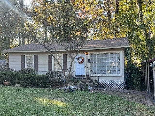 Single-story white house with a blue door, wreath, large front window, and a small yard in autumn light