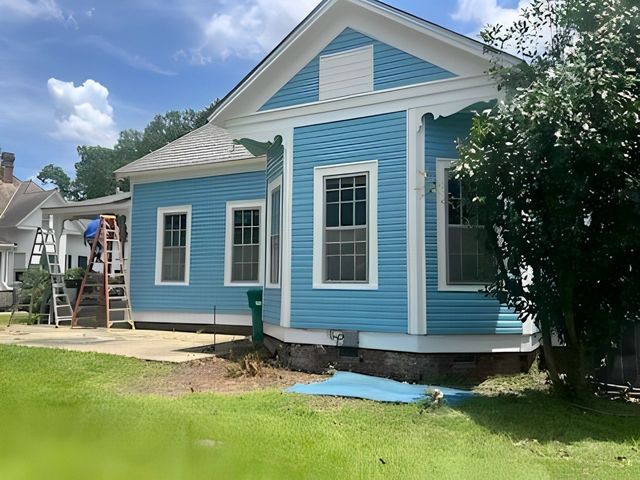 Blue house with white trim and a ladder in the yard under a partly cloudy sky