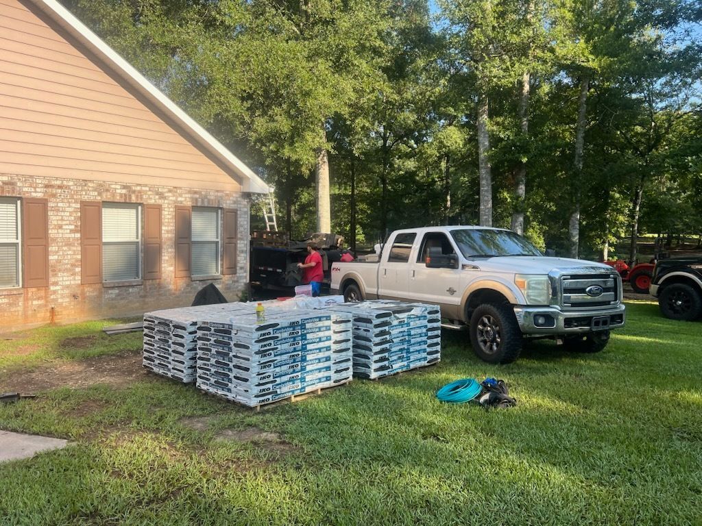 Stacks of bagged mulch beside a white pickup truck in a grassy yard next to a brick house.