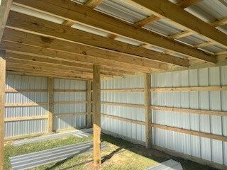 Empty wooden shed with corrugated metal walls and roof, sunlight casting shadows inside.