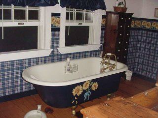 Clawfoot bathtub in blue room with floral accents, wood floor, and windows with blue drapes.