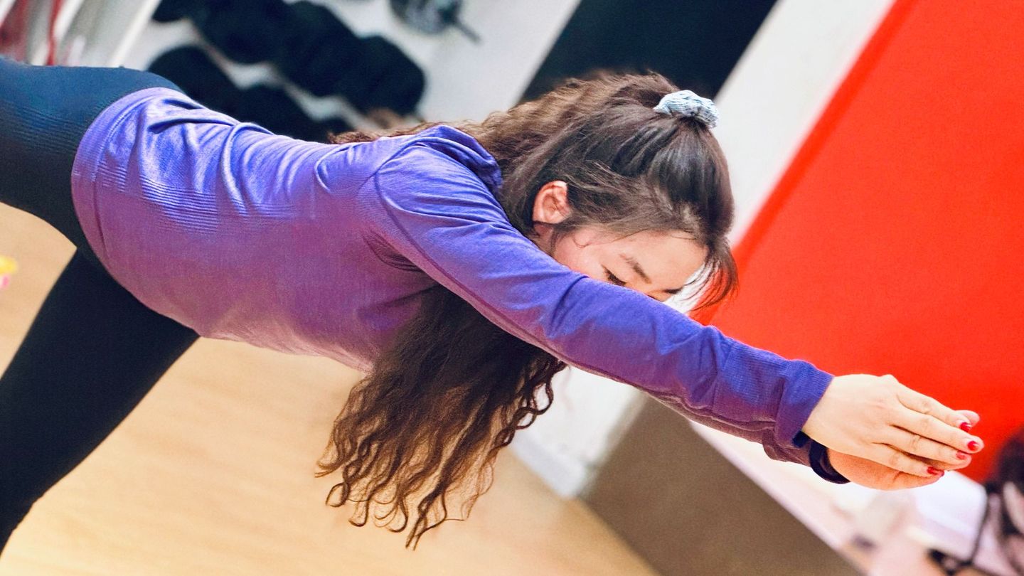 Move, feel and live better Woman in purple shirt stretching forward, hands clasped, in a dance studio.