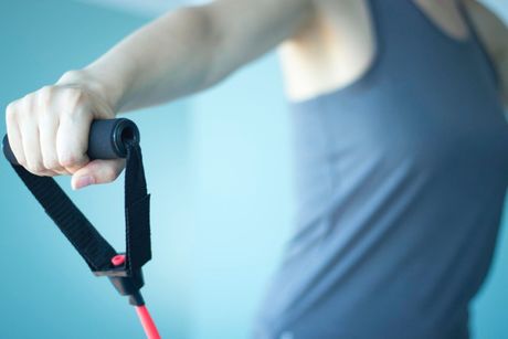Rehabilitation & Exercise Referral Person exercising with a resistance band, arm extended, wearing a gray tank top against a light blue background.