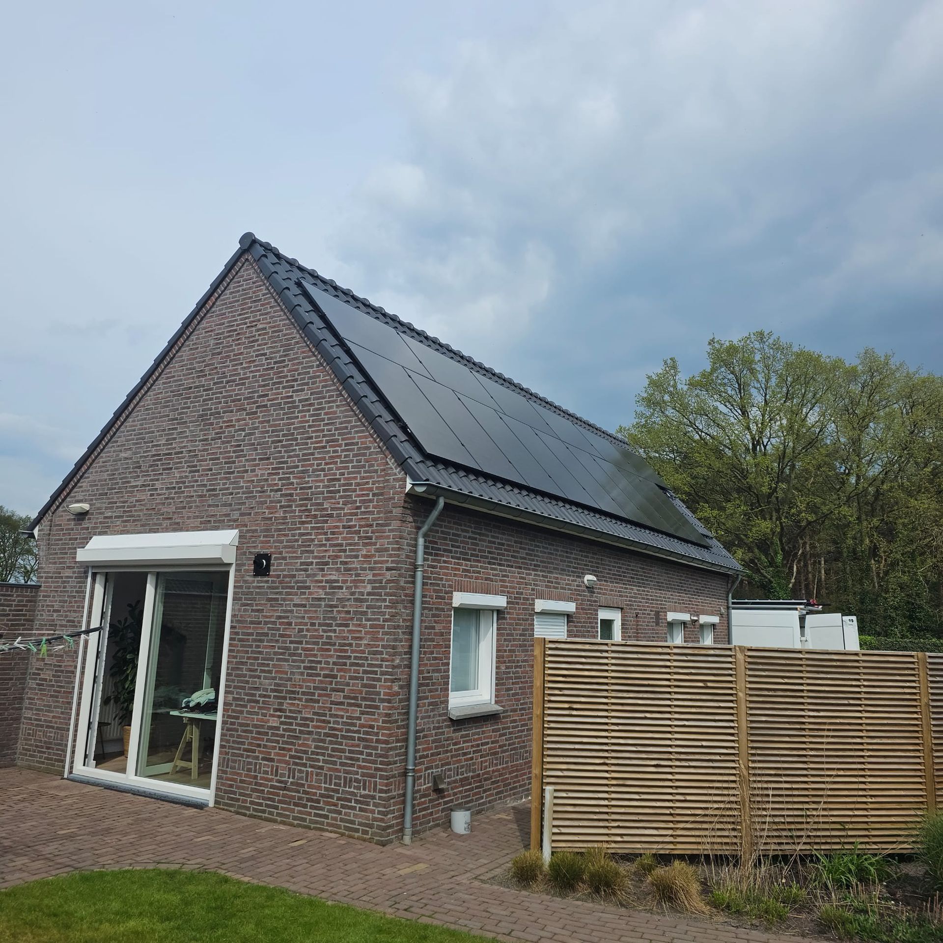 Bakstenen huis met zonnepanelen op het dak en een houten schutting. Bewolkte lucht.