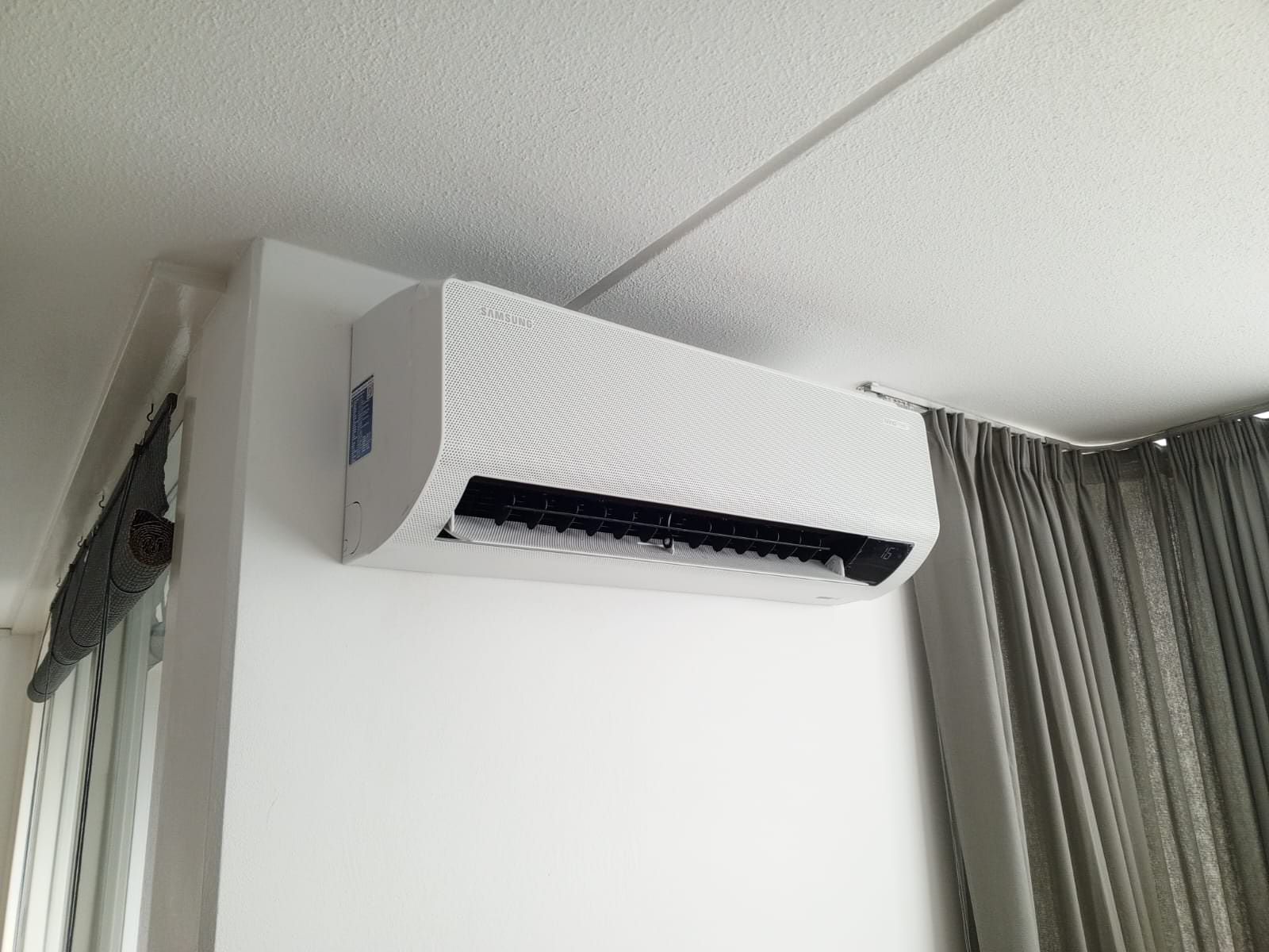 Witte, aan de muur gemonteerde airconditioner vlakbij een gordijn.