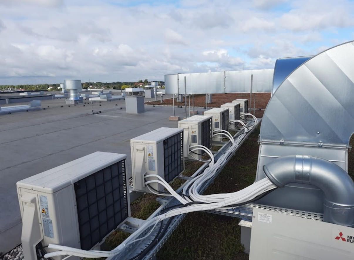 Uitzicht vanaf het dak op airconditioningunits, luchtkanalen en ventilatieopeningen op een plat dak onder een bewolkte hemel.