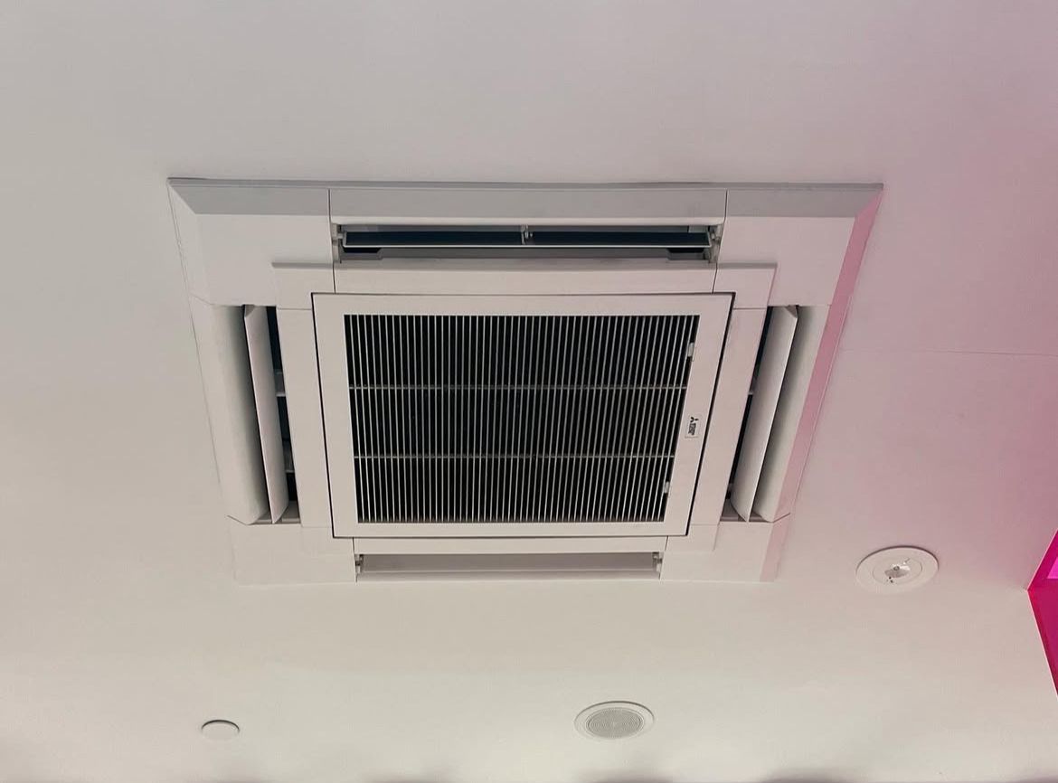 Witte plafondairconditioningunit met ventilatieopeningen en rooster, ingebouwd in het plafond.