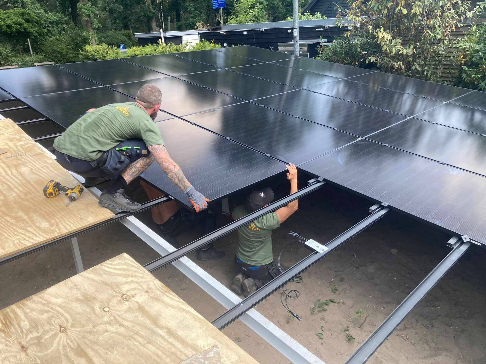 Twee arbeiders installeren zonnepanelen op een dak. Ze dragen groene shirts en de panelen zijn zwart.