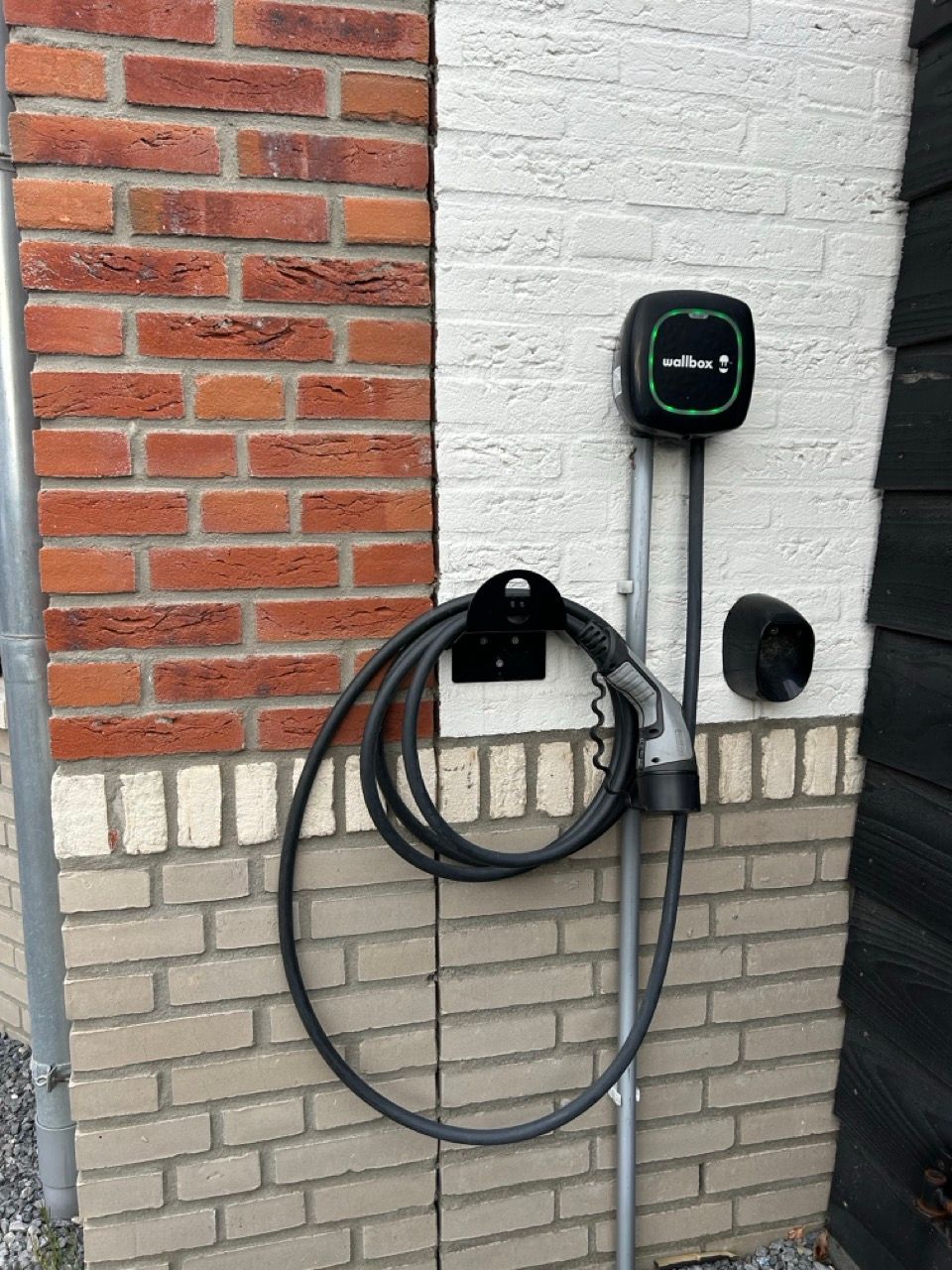 Oplader voor elektrische voertuigen aan een bakstenen en witte muur. Zwarte laadkabel opgerold.