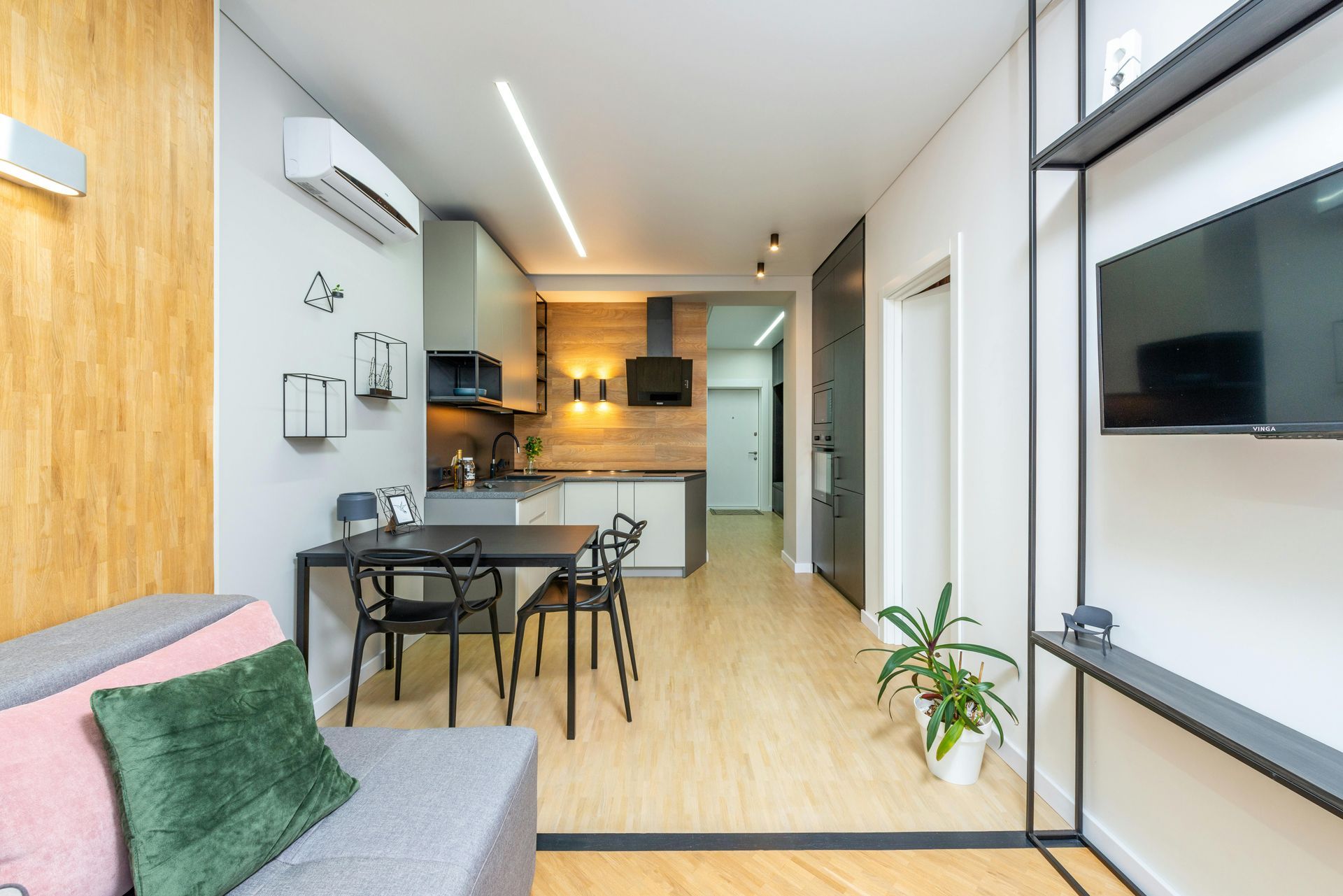 Klein, modern appartementinterieur met keuken, eethoek en tv op een plank.