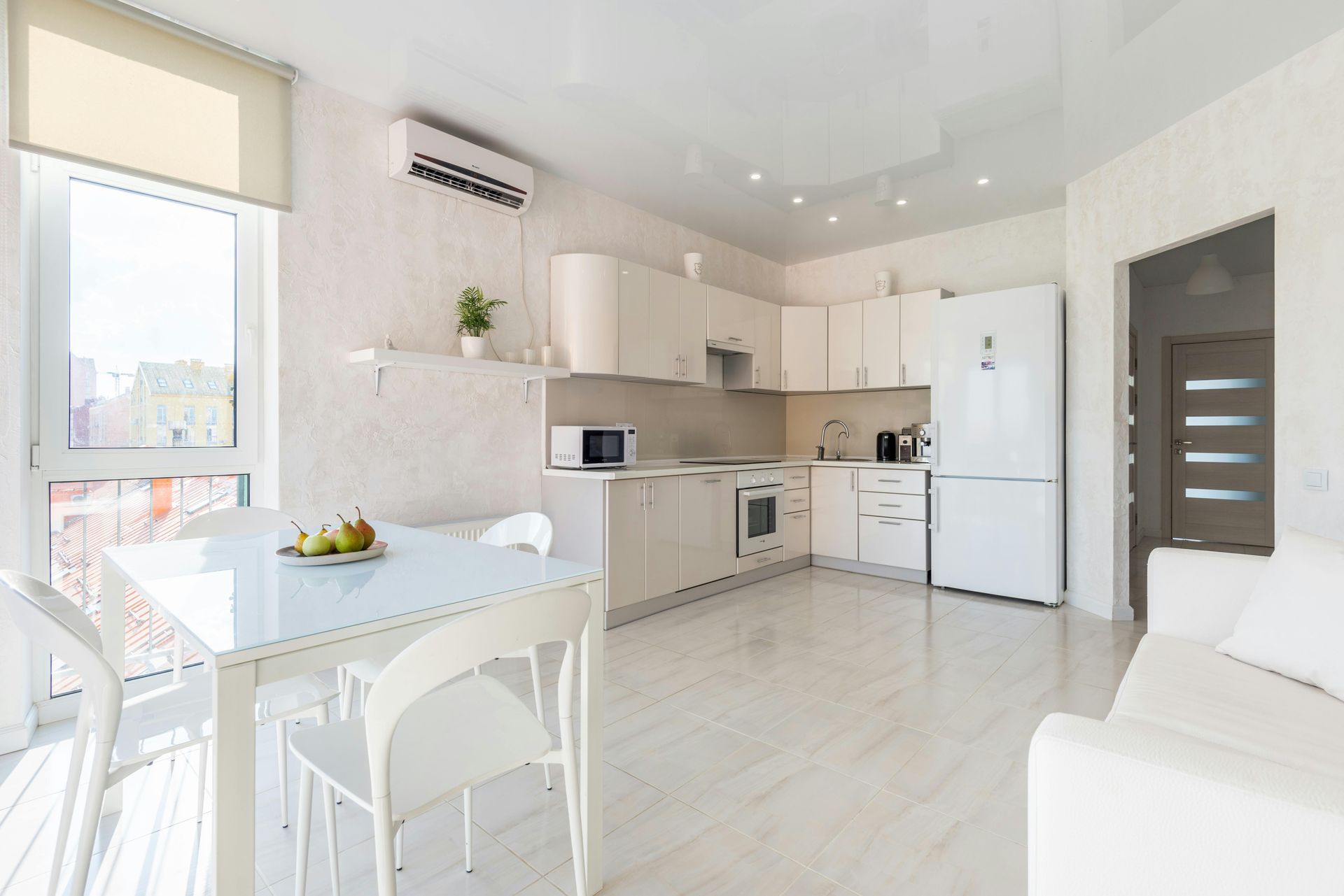 Moderne witte keuken en eethoek, met een tafel, stoelen, kasten en apparatuur.