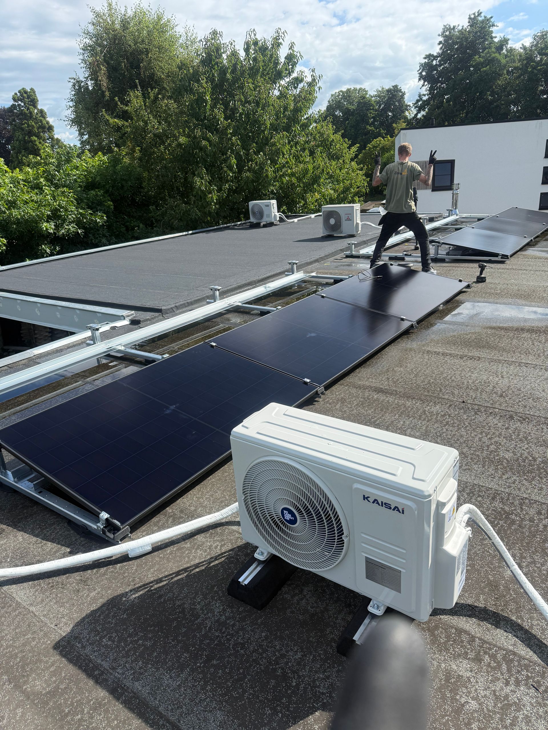 Een persoon werkt aan zonnepanelen op een plat dak naast een airconditioningunit.