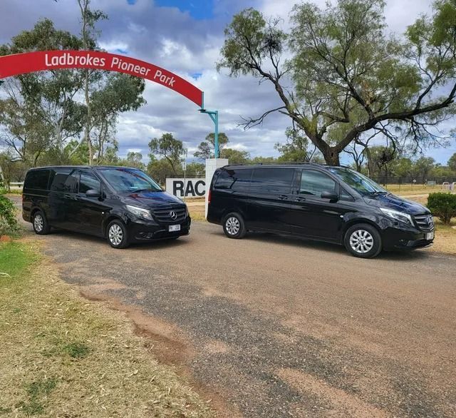 Two black vans parked at the Ludbrook Pioneer Park entrance on a grassy roadside under a cloudy sky — ASP Private Hire in Ross, NT